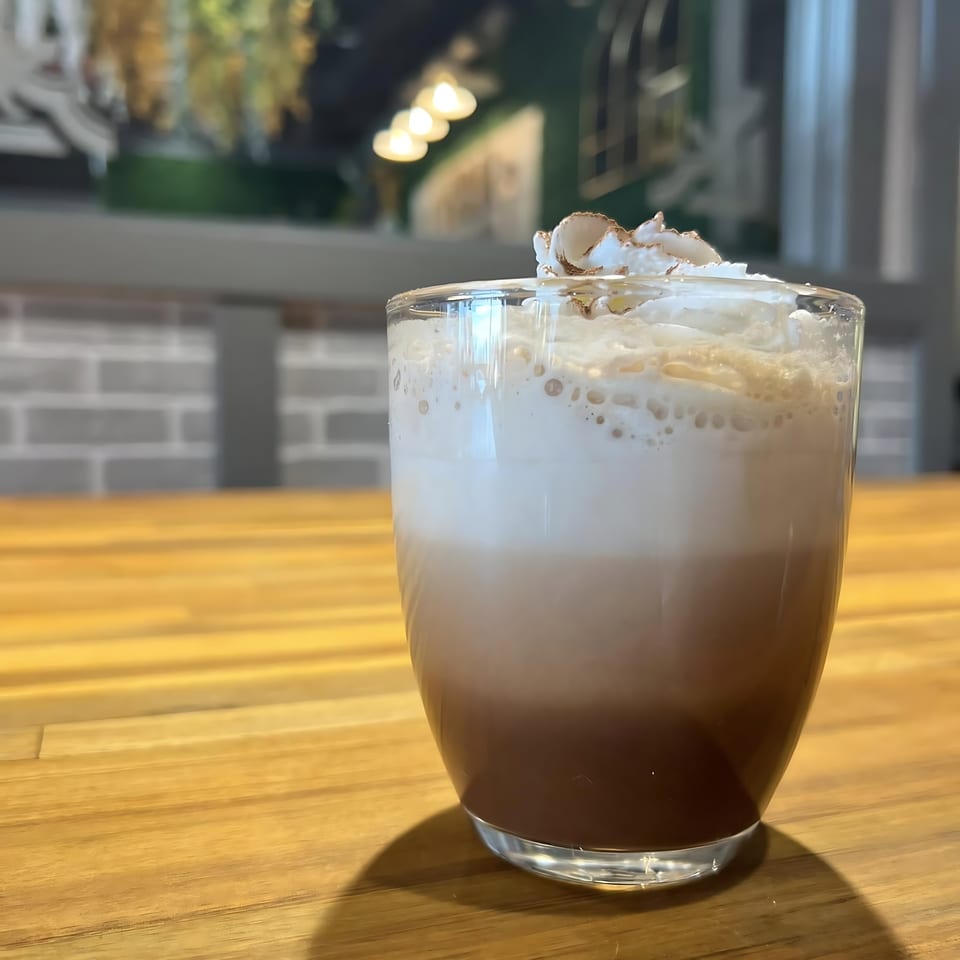 Thai iced coffee with whipped cream and cinnamon on a wooden table in a restaurant.