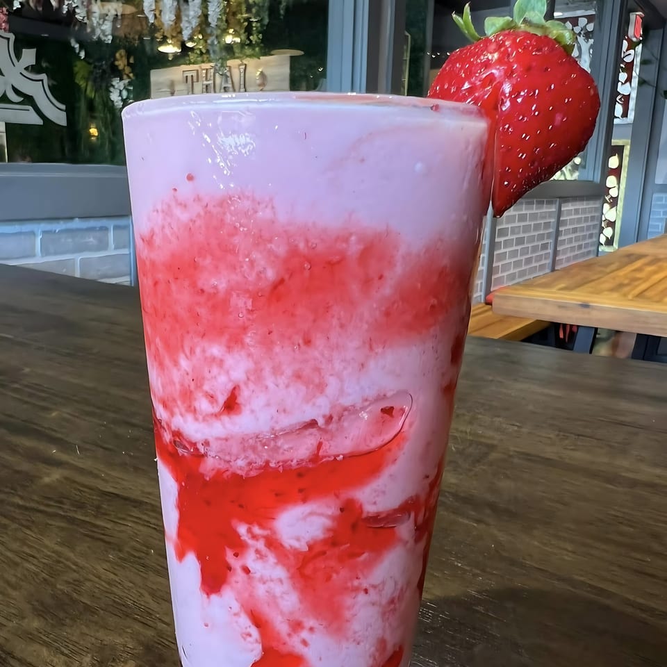 Strawberry smoothie with a whole strawberry garnish on a wooden table at Thai Bistro & Bar.
