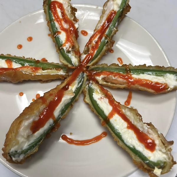 Six deep-fried jalapeno poppers filled with cream cheese and drizzled with red sauce, arranged in a star.