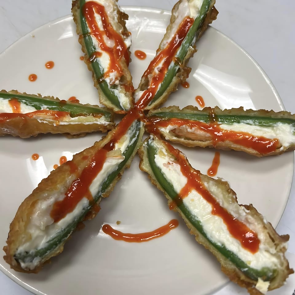 Six deep-fried jalapeno poppers filled with cream cheese and drizzled with red sauce, arranged in a star.