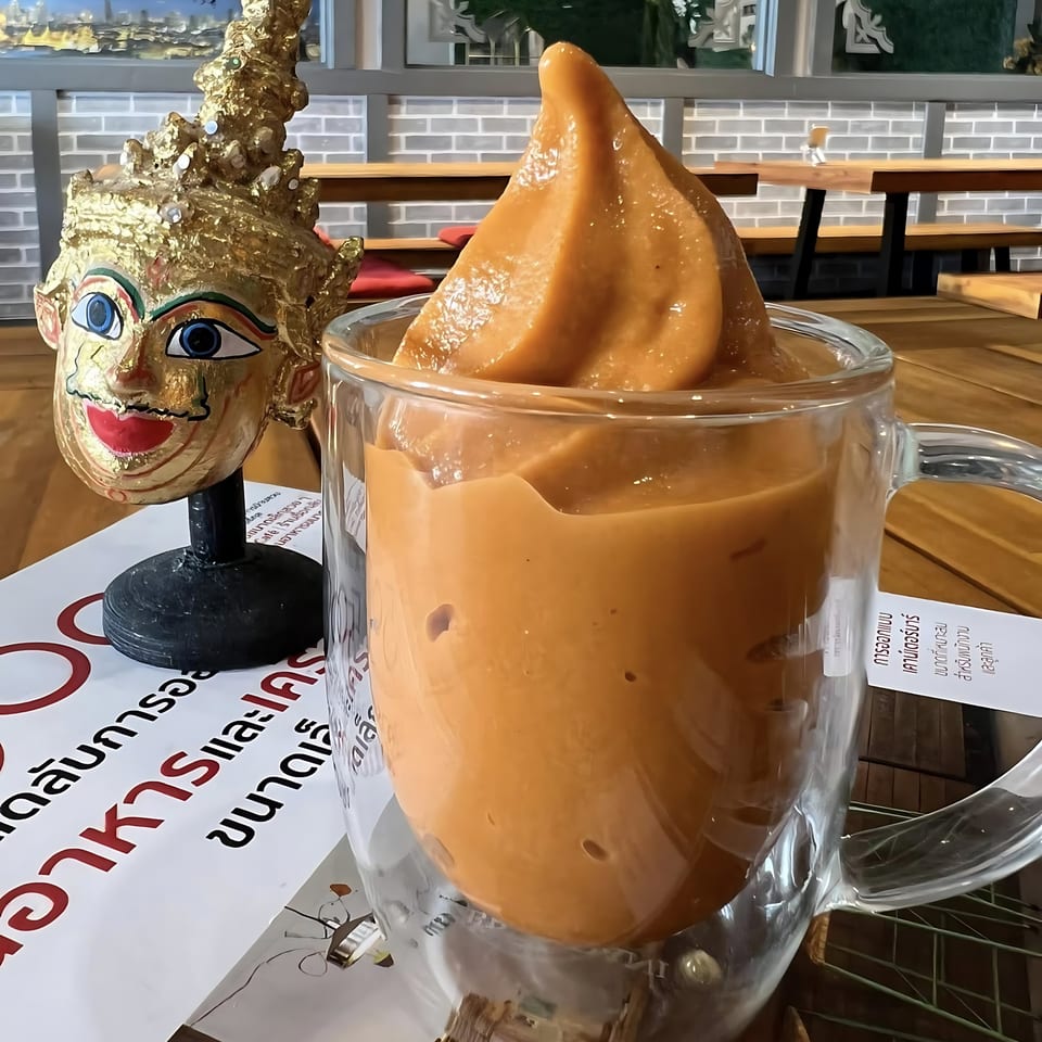 Thai iced tea smoothie in a glass mug next to a golden Thai statue on a table.