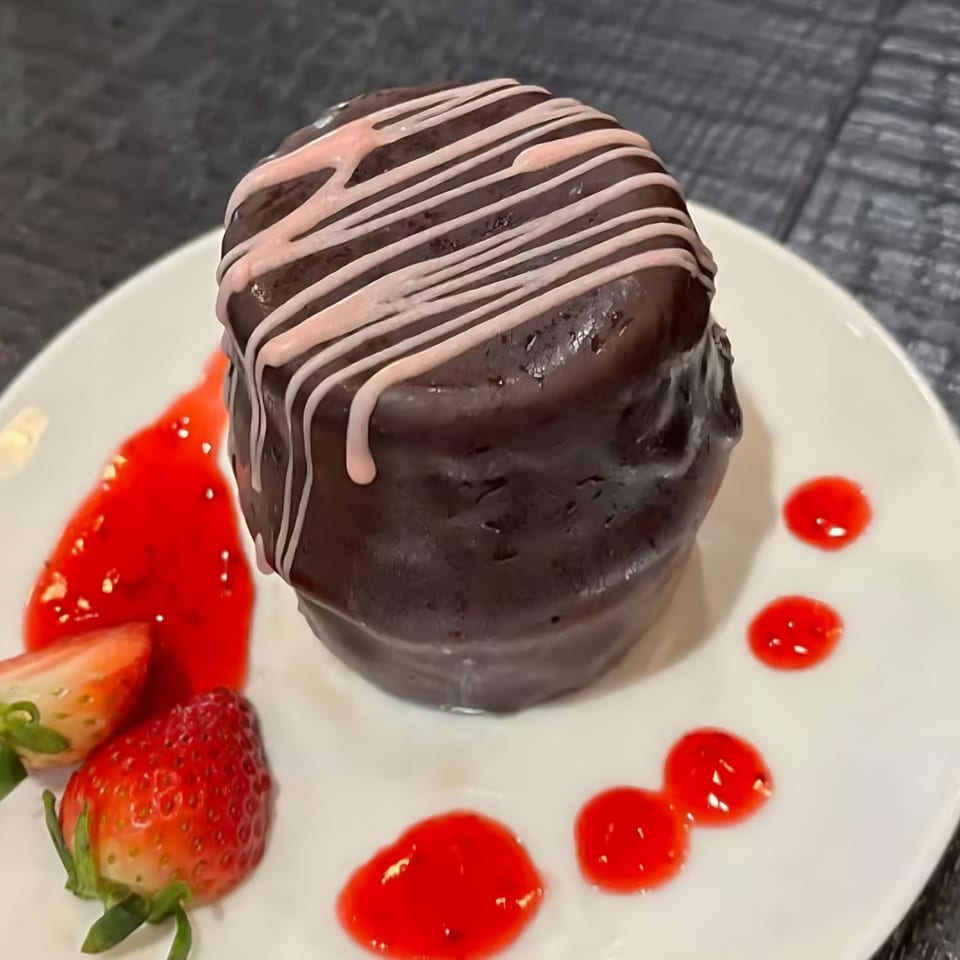 Chocolate lava cake with pink icing drizzle, strawberry sauce, and fresh strawberries on a white plate.