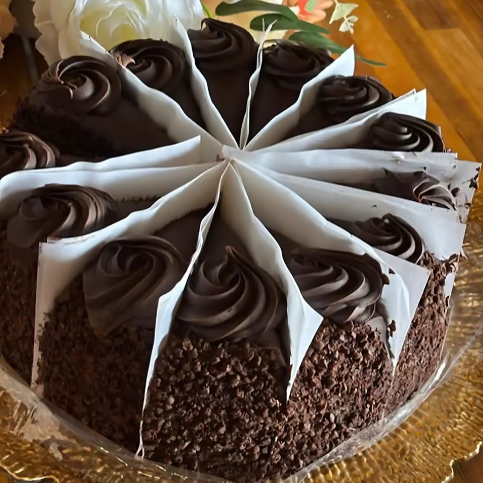 A chocolate cake with chocolate frosting swirls, divided into slices by white paper, on a golden plate.