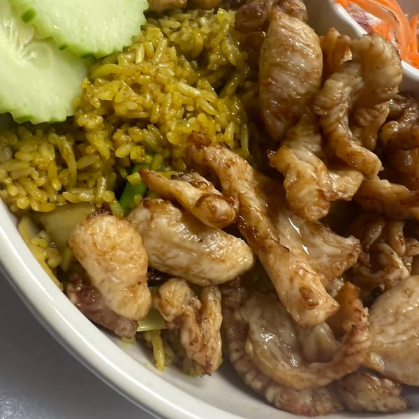 Close-up of Thai yellow curry rice with sliced chicken and cucumber in a white bowl.