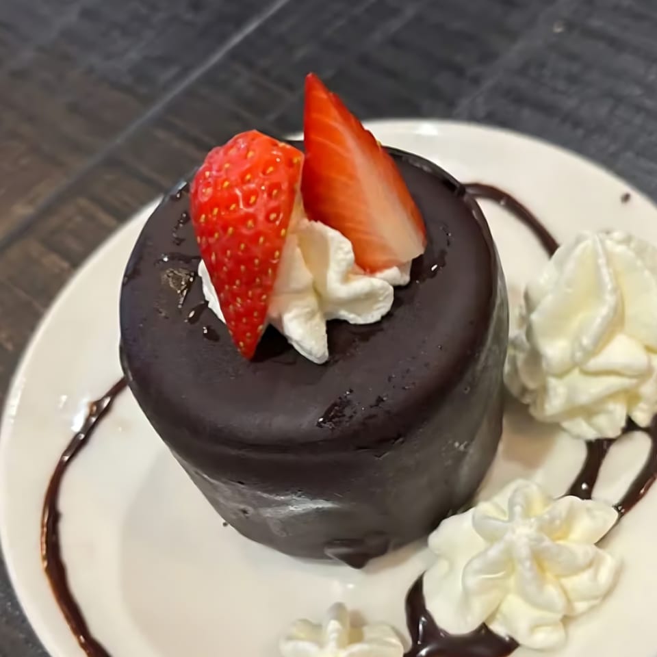Chocolate lava cake topped with strawberries and whipped cream, drizzled with chocolate syrup.
