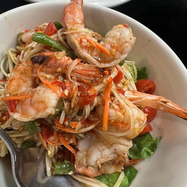 Spicy Thai shrimp salad with green papaya, tomatoes, and long beans in a white bowl.