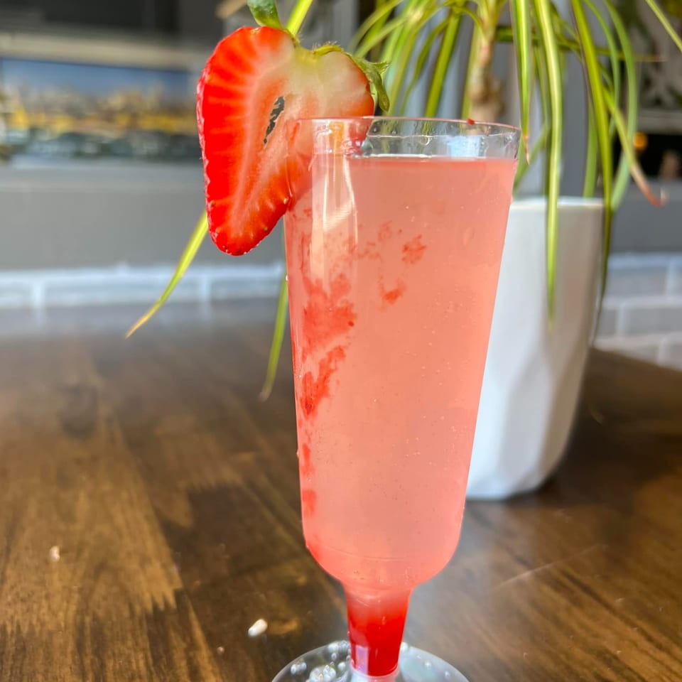 Pink strawberry drink in a tall glass, garnished with a sliced strawberry, on a wooden table.