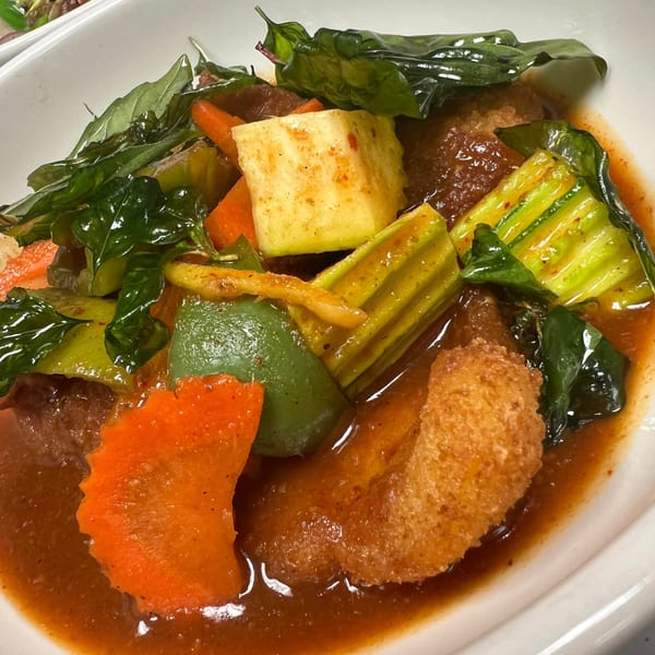Close-up of a Thai dish with fried tofu, carrots, zucchini, bell peppers, and basil in a rich sauce.