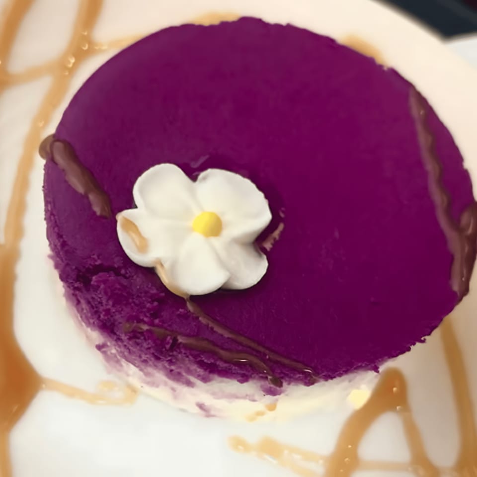 Purple dessert with a white flower and yellow center, drizzled with chocolate and caramel.